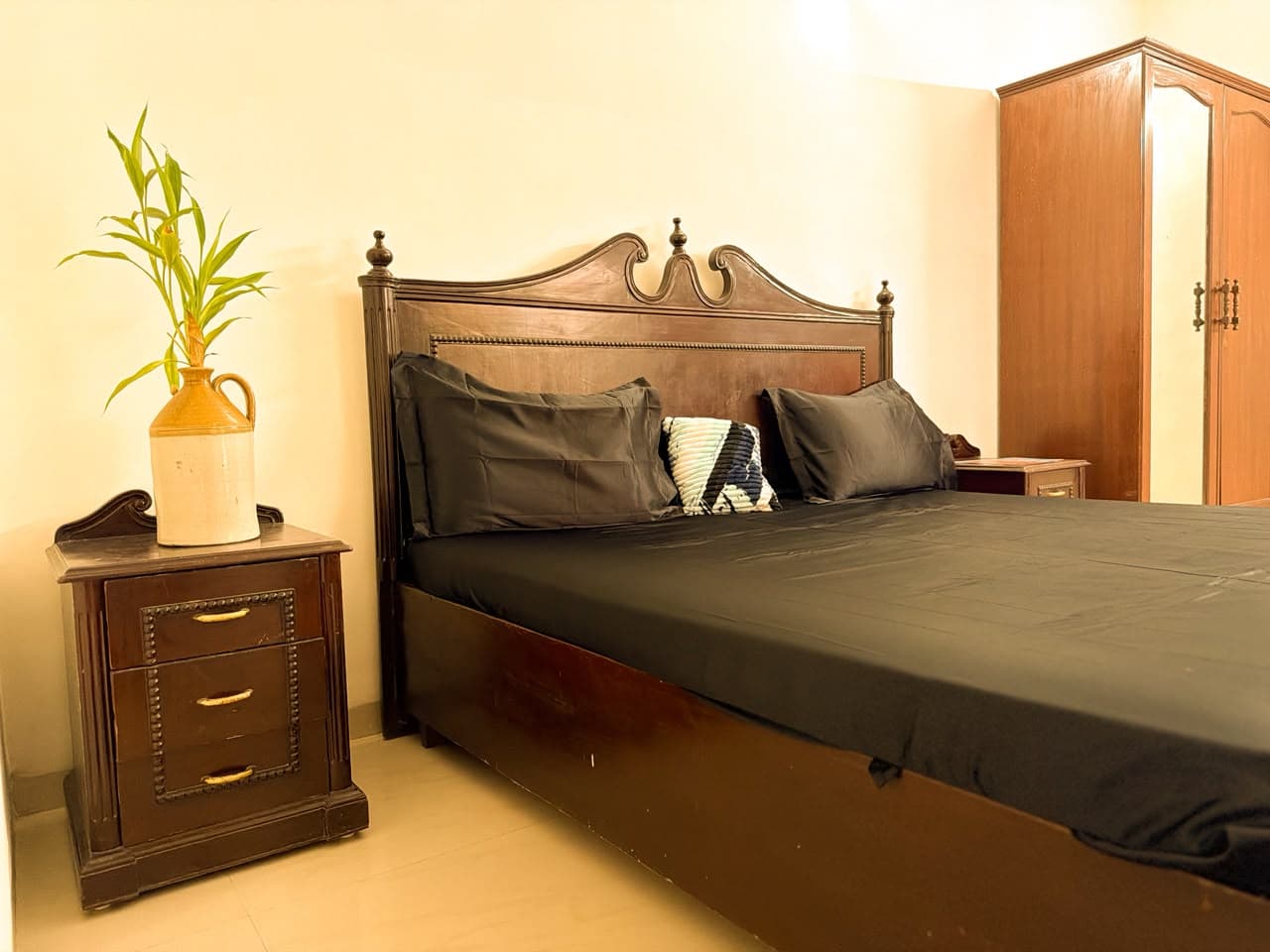 Carved teak headboard, charcoal pillows and a bedside chest with a bamboo plant