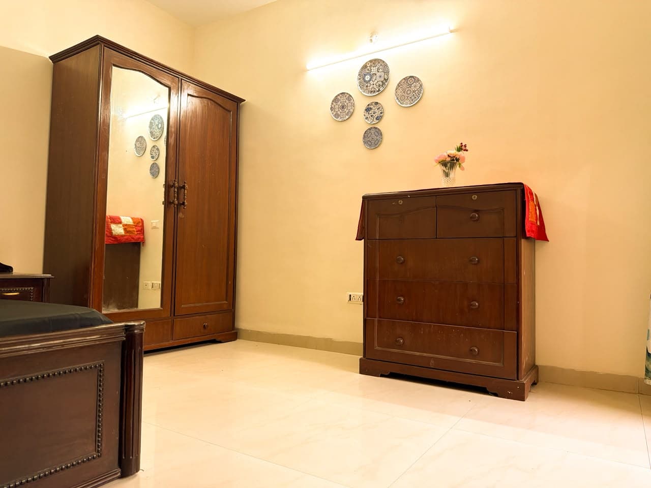 Teak wardrobe with a full-length mirror beside a chest of drawers under decorative wall plates