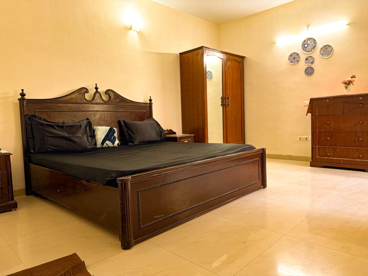 Main bedroom with a carved teak bed in charcoal linen, a mirrored wardrobe and blue painted plates on the wall