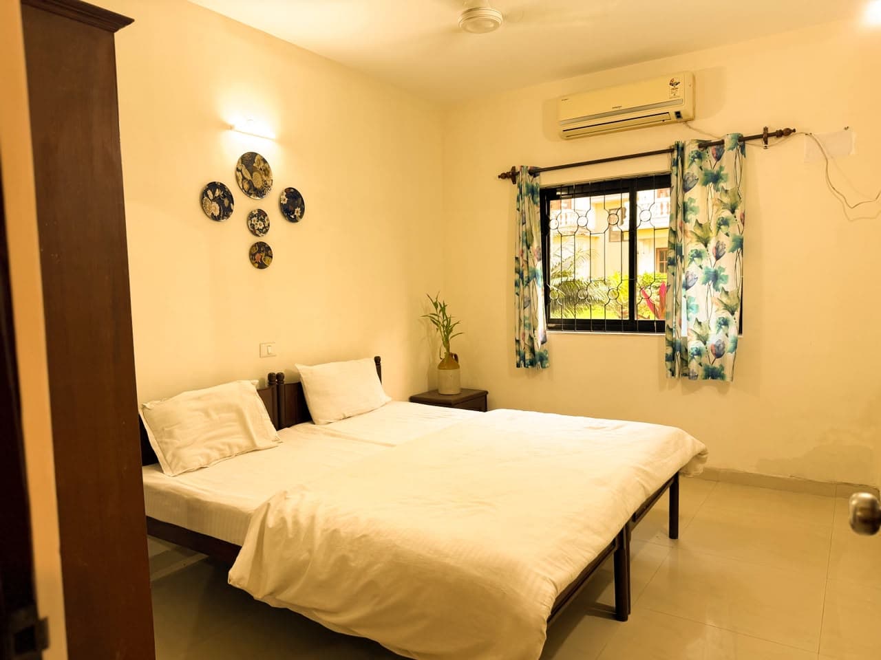 Second bedroom with two beds in white linen, air-conditioning and botanical-print curtains